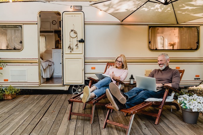 Camper with man and woman relaxing in front of it