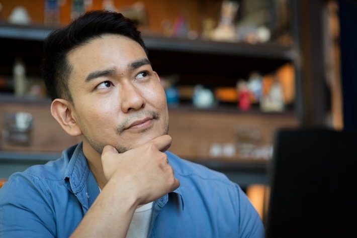 Asian man in deep thought closeup in profile with laptop.